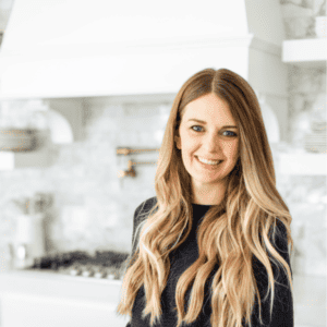 Friendly woman smiling in a modern kitchen, promoting booking appointments for wellness services at Root and Leaf Wellness.