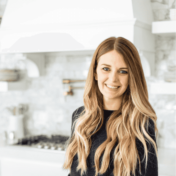 Friendly woman smiling in a modern kitchen, promoting booking appointments for wellness services at Root and Leaf Wellness.